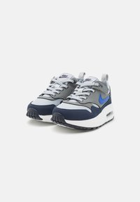 Sneakers Nike con una toma grigia e accenti blu, suola intermedia bianca e suola esterna nera. Il design include lacci e un linguetta posteriore.