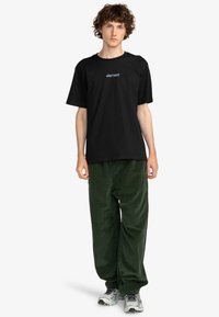 Camiseta de algodón negra con el logo "element" en azul, combinada con pantalones de pana verde oscuro y zapatillas grises.