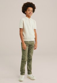 Beige textuur polo-shirt met een kraag, gecombineerd met olijfgroene slim-fit broek en witte sneakers met veters.