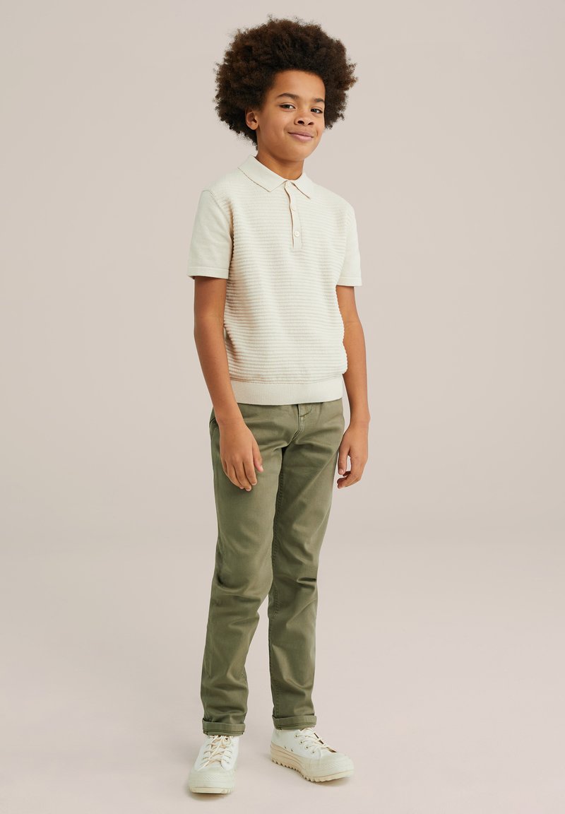 Beige textuur polo-shirt met een kraag, gecombineerd met olijfgroene slim-fit broek en witte sneakers met veters.