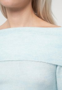Jasnoniebieski sweter dzianinowy z odsłoniętymi ramionami, wyróżniający się wyraźną fakturą i luźnym krojem. Subtelne wariacje kolorystyczne zwiększają jego wizualne zainteresowanie.