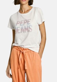 Camiseta blanca de algodón con el texto multicolor "PEPE JEANS" en strass. Combinada con pantalones sueltos de color durazno con cintura elástica.