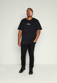 Černé bavlněné tričko s nápisem „COSMIC MYSTERY“ v bílé barvě, kombinované s černými úzkými džíny a černými botami. Jednoduchý design, neutrální barvy.