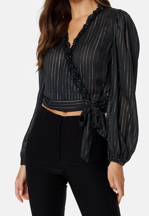 Zwarte wikkelblouse met verticale zilveren strepen, geplooide V-hals, lange ballonmouwen en zijstrik, gecombineerd met zwarte broek.