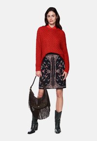 Red knit sweater, floral-patterned black skirt, brown fringe handbag, and black heeled boots. Textured materials with layered design.