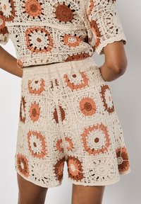 Pantaloni corto all'uncinetto beige con motivi floreali arancioni e marroni. Presentano un design a trama aperta testurizzata ed una vita elastica.