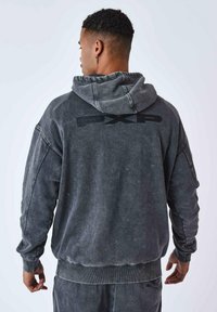 Sweat-shirt à capuche gris avec une finition usée, arborant un logo noir au dos, des poignets côtelés et un tissu texturé.