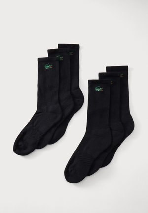 Sechs schwarze gerippte Socken mit einem kleinen grünen und roten bestickten Krokodil-Logo nahe dem oberen Bündchen auf weißem Hintergrund.