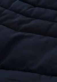 Nahaufnahme von dunkelmarineblauem, gestepptem Stoff mit horizontalen Nähten und gepolsterten Abschnitten, wahrscheinlich Teil einer Jacke oder eines Mantels.