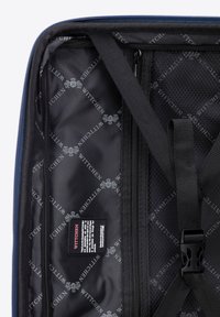 Intérieur noir d'un sac de voyage avec un motif de logo répété, des compartiments zippés et des sangles ajustables pour sécuriser les objets.