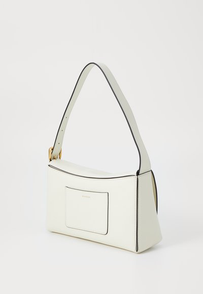 White leather handbag with black trim, triangular shape, short strap, front pocket, and gold hardware accent. Smooth texture, minimal design.