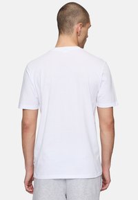 Camiseta de algodón blanca de manga corta, con cuello redondo y bajo recto. Diseño minimalista, sin patrones ni acentos visibles.