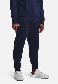 Sudadera azul marino con un bolsillo frontal y puños acanalados, combinada con pantalones jogger a juego. Presenta un logo blanco en el muslo izquierdo.
