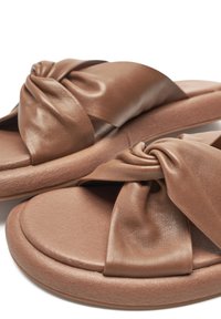 Brown slide sandals featuring a knotted, soft synthetic upper, padded footbed, and round sole with a textured finish.