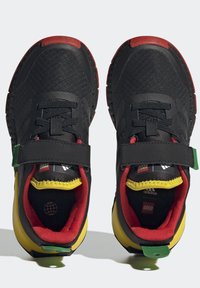 Svarta sportskor med röda och gula accenter, med en strukturerad överdel, kardborreband och en grön hälflik för extra stöd.