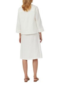Witte katoenen outfit bestaande uit een losvallend lange mouwen shirt en een knie-lange rok. Gelaagde stof, eenvoudig ontwerp en geen zichtbare patronen.