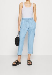 Jasnoniebieskie, luźne spodnie cargo z elastycznym pasem i sznurkiem, wyposażone w boczne kieszenie. Połączone z białym topem na ramiączkach i czarnymi dodatkami.