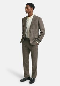 Giacca di suit a spina di pesce marrone con pantaloni coordinati, abbinata a una camicia chiara. Scarpe in pelle nera completano l'outfit.
