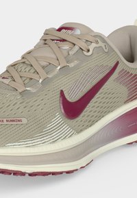 Μπεζ και μπορντό αθλητικό παπούτσι Nike για τρέξιμο με άνω μέρος από δίχτυ, μαλακή σόλα και μπεζ κορδόνια, με εμφανές το λογότυπο στο πλάι και υφασματικές λεπτομέρειες.