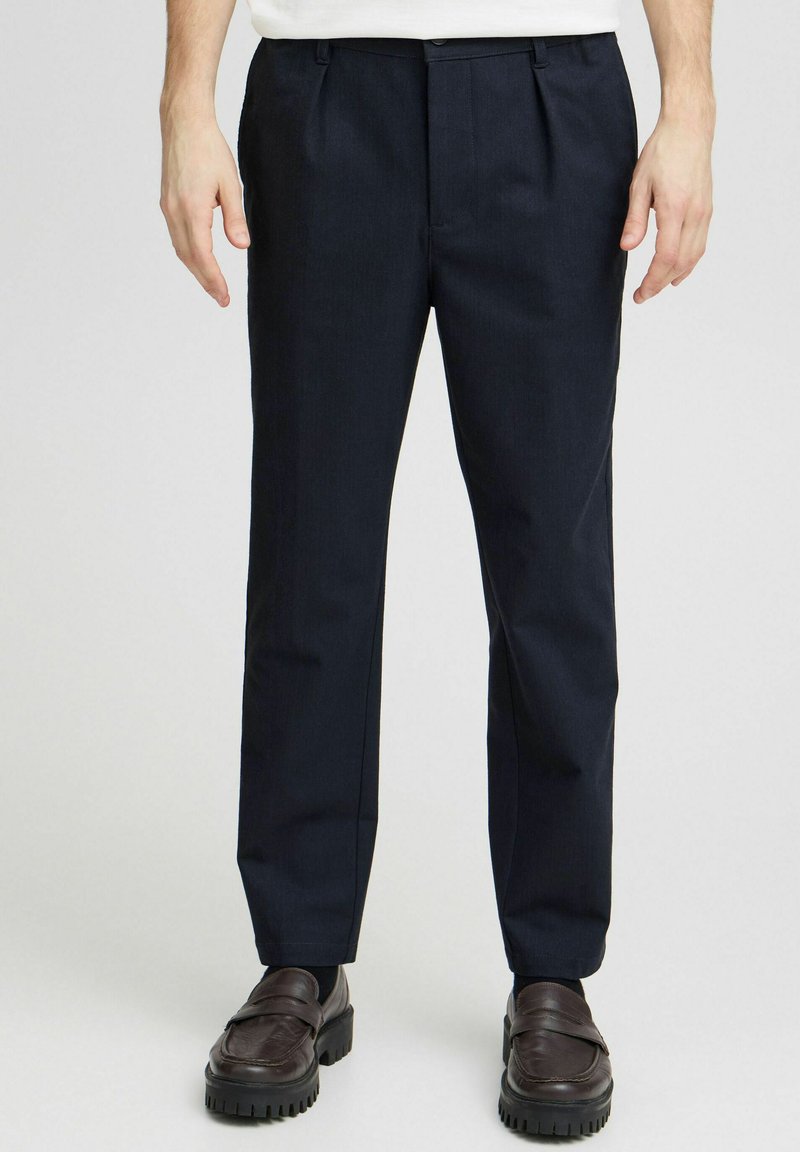 Pantalons tailleur bleu marine avec un devant plat, fabriqués en tissu texturé. Dotés d'une coupe droite et de poches latérales, associés à des mocassins marron.