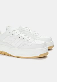 Sneaker bianche in pelle con finitura testurizzata, dotate di lacci rotondi, logo con tre strisce e una suola in gomma spessa. Perforazioni sulla punta.