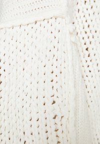 Weißer gestrickter Stoff mit einem strukturierten Muster und lockeren Maschen. Weiche Textur mit leichten Variationen in der Dicke.