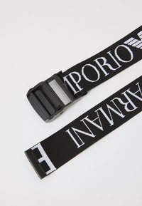 Curea din material textil negru cu un model de text alb "Emporio Armani", dotată cu o cataramă din plastic și o textură plată țesută, potrivită pentru diverse ținute.