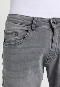 Vaqueros de mezclilla gris con un corte clásico, que cuentan con un bolsillo frontal, costuras contrastantes y un botón de metal en la cinturilla.
