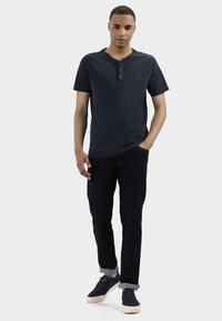 T-shirt Henley à manches courtes marine avec patte de boutonnage à trois boutons, associé à un jean foncé et des baskets ; coupe décontractée et texture uniforme.