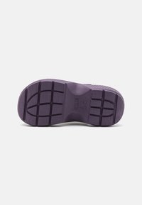 Semelle en caoutchouc violette avec une surface texturée présentant un motif en grille pour l'adhérence, des zones lisses et des détails de marque en relief.