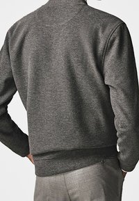 Harmaa fleece-huppari korkealla kauluksella, ribbireunuksilla hihoissa ja vyötäröllä. Sillä on sileä pinta ja rento istuvuus, ja takakuvassa on pelkkä tausta.