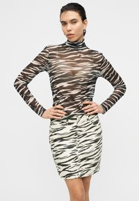 Καφέ και μπεζ μπλούζα με ρίγες τίγρης, με μακριά μανίκια και ψηλό γιακά, συνδυασμένη με mini φούστα με ρίγες τίγρης στον ίδιο σχεδιασμό, που αναδεικνύει εφαρμοστή γραμμή.