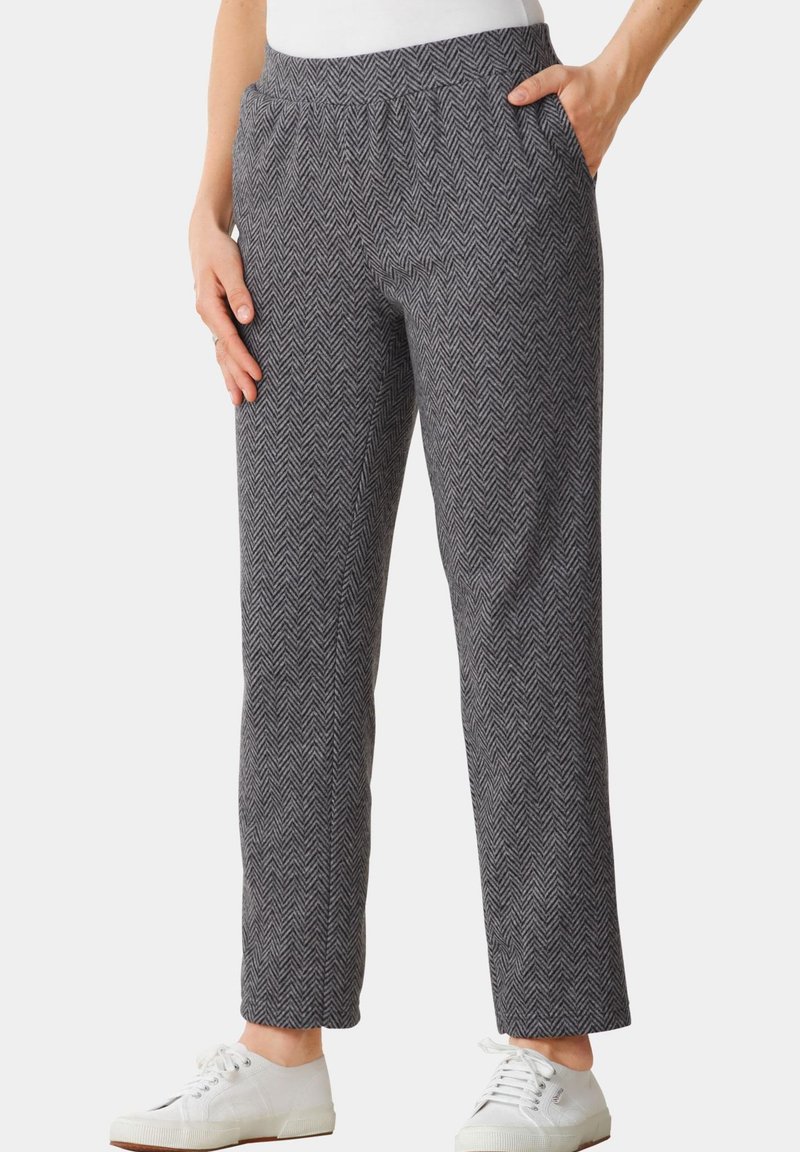 Pantalon à motif chevron gris avec une taille élastique, des poches latérales et des jambes droites, associé à des baskets blanches.