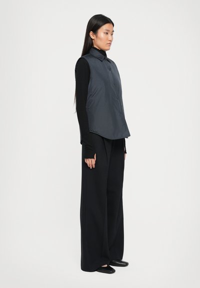 Polstret vest i mørkegrå med krage, knapp foran og løs passform, parret med svarte vide bukser. Glatt tekstur, minimal design.
