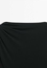 Tissu noir étiré horizontalement sur un fond blanc uni, montrant une texture lisse et de légères plis sur le côté gauche.