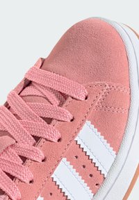 Rosa Wildledersneaker mit strukturierter Oberfläche, weißer Gummisohle und geflochtenen Schnürsenkeln. Verfügt über drei weiße Streifen und ein Zickzack-Muster an der Seite.