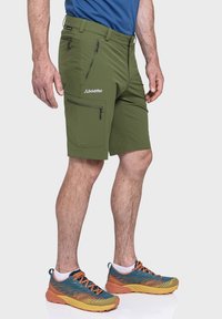 Grüne Outdoor-Shorts aus leichtem, schnell trocknendem Material, mit mehreren Reißverschlusstaschen und einem Logo auf der Vorderseite.
