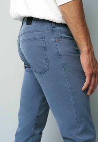 Jean en denim bleu clair avec une coupe ajustée. Les caractéristiques comprennent une poche arrière, des coutures contrastantes et une étiquette noire au niveau de la taille.