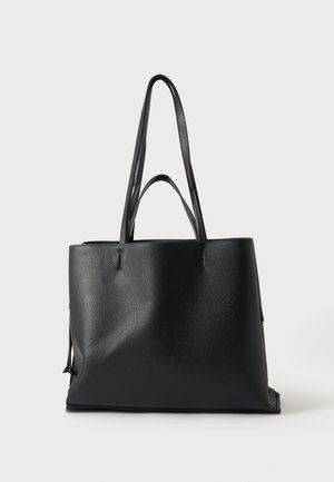 Bolso tote de cuero negro con dos asas largas para el hombro y dos asas más cortas para la mano sobre un fondo liso y claro.