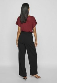 Haut court maroon associé à un pantalon large noir. La tenue présente une coupe décontractée et une texture de tissu lisse. Des chaussures à talons marron à lanières complètent le look.