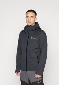 Veste imperméable noire avec un col haut, capuche réglable, fermeture éclair avant et poches latérales. Présente un logo sur la poitrine et le bras.