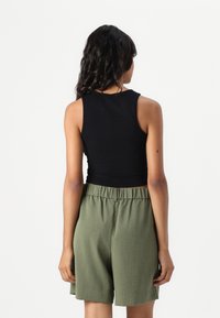Black, sleeveless crop top with a round neckline paired with loose, olive-green shorts featuring an elastic waistband and side pockets.