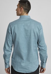 Light blue button-up shirt made of soft fabric, featuring a classic collar, long sleeves, and a curved hem with buttoned cuffs.