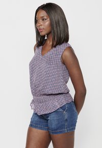 Mouwloze top met v-hals in een roze en blauwe bloemenprint; lichtgewicht stof met een gebogen zoom, gecombineerd met strakke denim shorts.