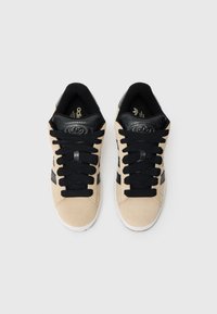 Μπεζ σουέτ αθλητικά παπούτσια με μαύρες λεπτομέρειες, με χοντρές μαύρες κορδόνια και υφασμένο μαύρο τακούνι. Λευκή λαστιχένια σόλα και ελάχιστο λογότυπο.