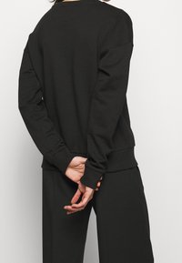 Sudadera negra de gran tamaño con cuello redondo y mangas largas, con puños y bajo acanalados. Tejido suave con una textura lisa.