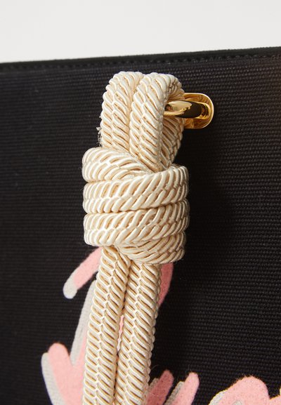 Black fabric bag with cream-colored braided rope detail secured with a gold hardware clasp, featuring pink abstract patterns on the front.