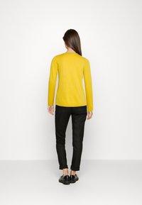 Geel pullover trui met lange mouwen, een gladde textuur en een ronde zoom, gecombineerd met zwarte broek en zwarte schoenen.