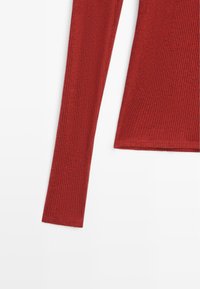 Top a maniche lunghe a coste in rosso scuro. Presenta un design aderente con una texture sottile e un orlo dritto.