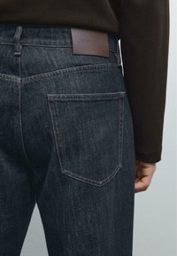 Dunkelblaue Jeans mit gerader Passform, ausgestattet mit einem Leder-Branding-Patch, sichtbaren Nähten und zwei hinteren Taschen im klassischen Design.